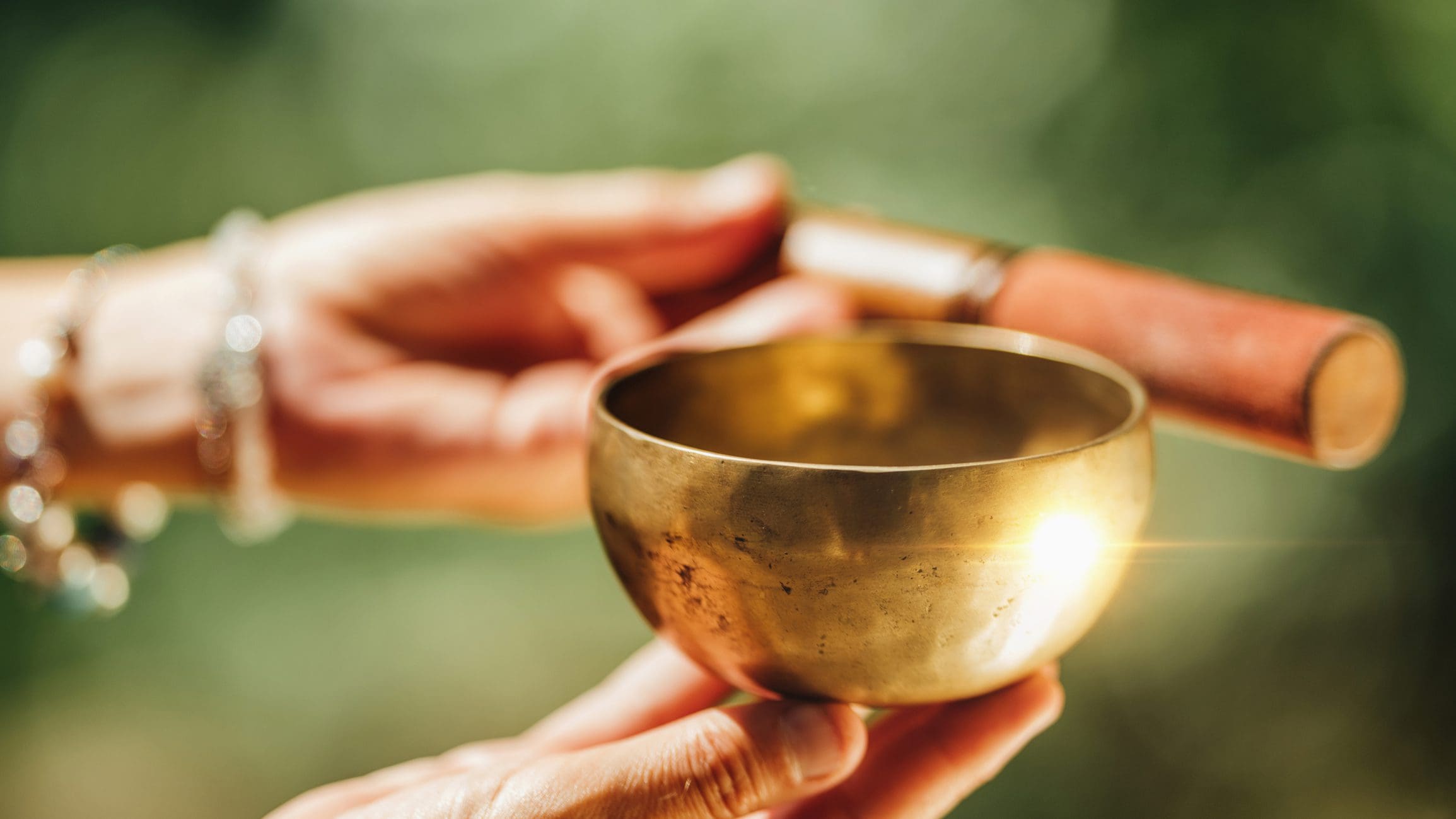 Hands holding a singing bowl and mallet.