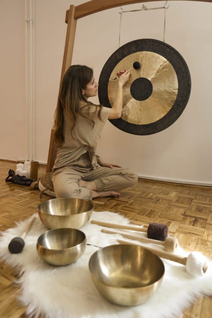 Woman playing gong with singing bowls nearby.